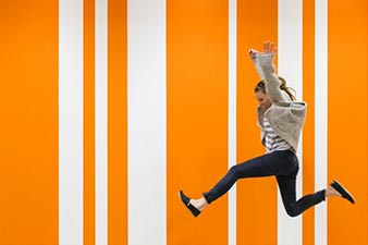 Woman leaping in front of an orange striped backdrop