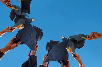 Students lifting graduation caps up towards the blue sky
