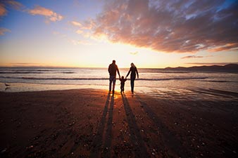 Young parents with small child on the beach at sunset
